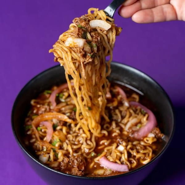 A hand lifts a forkful of ramen noodles with meat and onions from a black bowl.