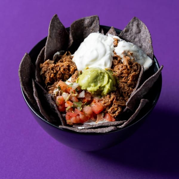 A black bowl of nachos with shredded meat, guacamole, sour cream, and pico de gallo.