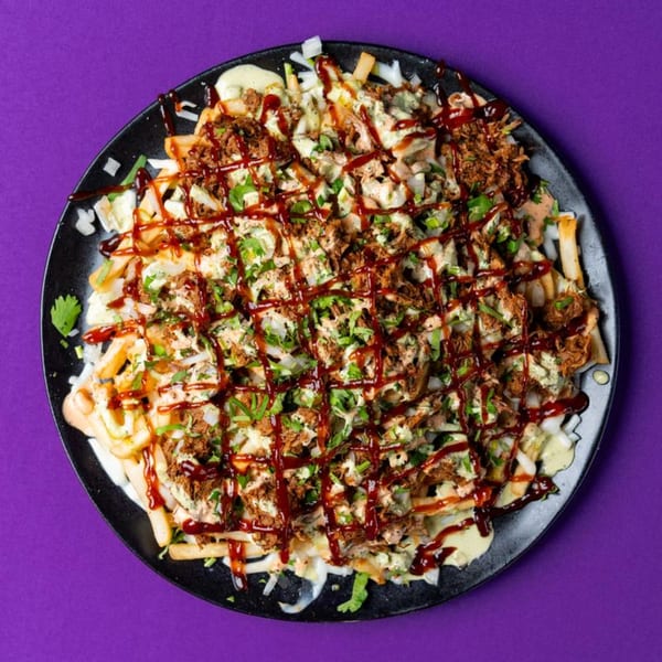 Loaded fries topped with pulled pork, white sauce, BBQ sauce, and fresh herbs on a black plate.