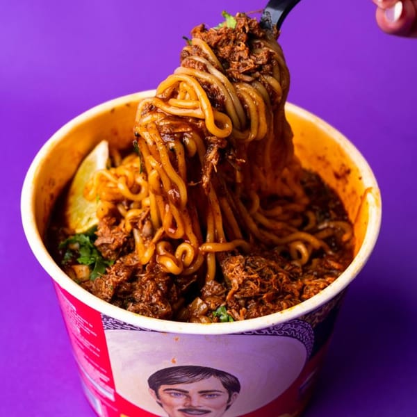 A fork lifts saucy noodles and shredded meat from a branded cup against a purple background.